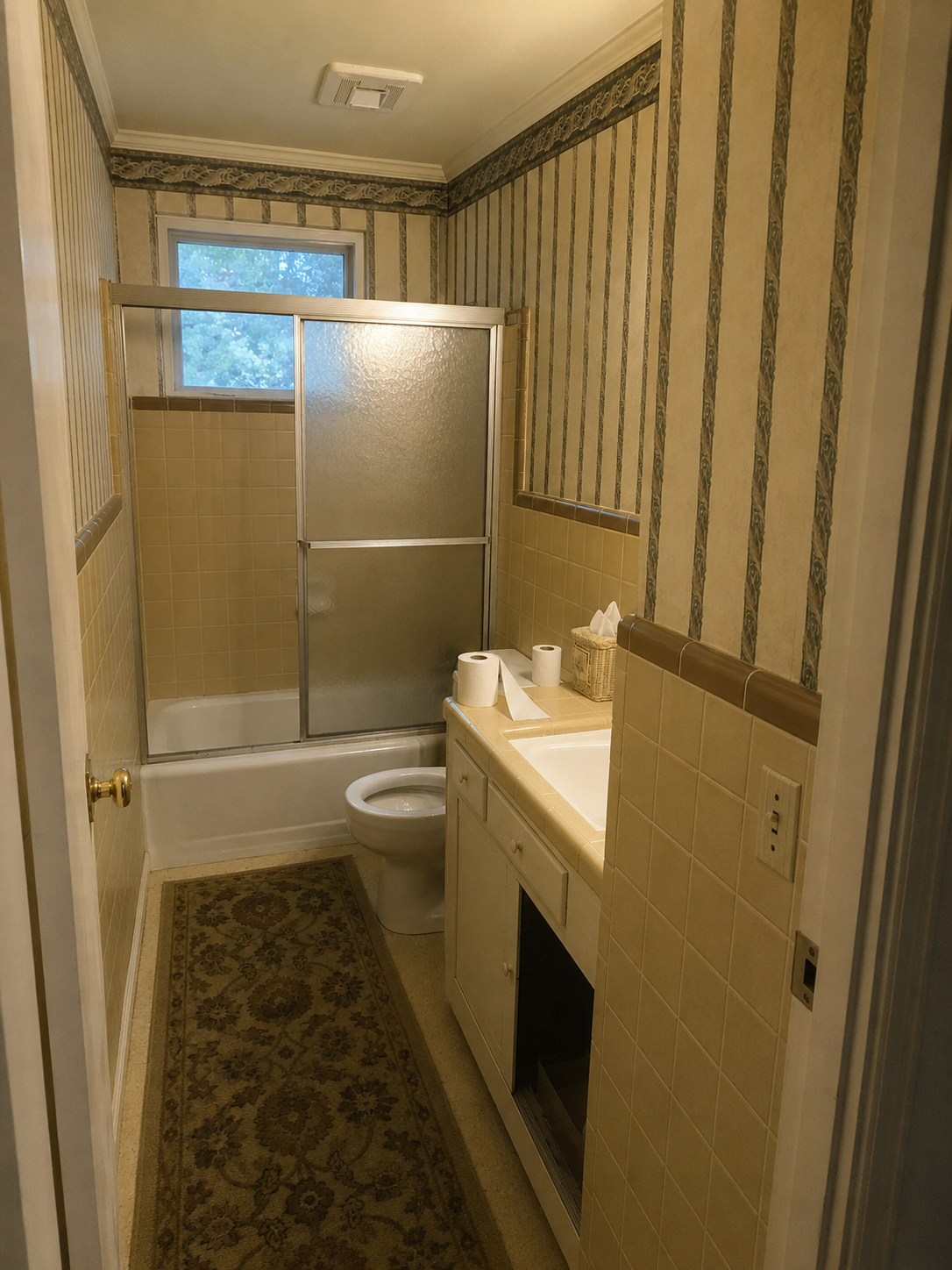 Bathroom with dated striped wallpaper and beige tile before remodel