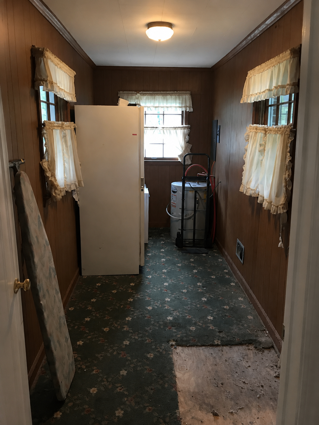 Dated room with dark wood paneling, ruffled curtains, and floral carpet before refresh